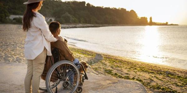 Hombre en silla de ruedas en la playa acompañado de una mujer