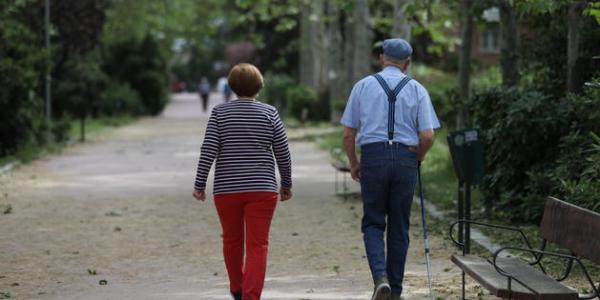 Una mujer y un hombre de edad avanzada con bastón caminando. EP