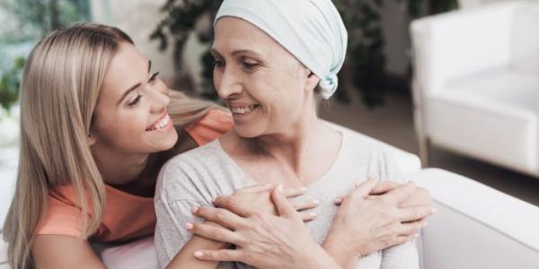 Una mujer con cáncer está sentada en un sofá blanco al lado de su hija 