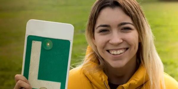 Una joven posa sonriente con la L tras aprobar el examen de conducir.