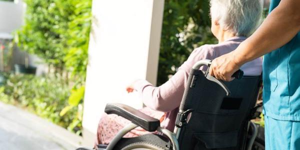 Un cuidador llevando a una mujer discapacitada en silla de ruedas