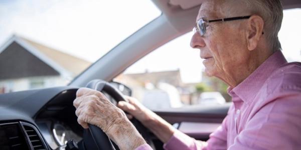 Persona mayor sentado ante el volante de un vehículo 