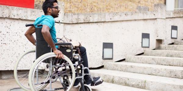 Hombre con discapacidad en silla de ruedas esperando en la parte inferior de una escalera