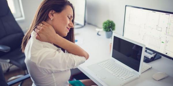 Mujer con dolores musculares trabajando con su ordenador / Objetivo bienestar