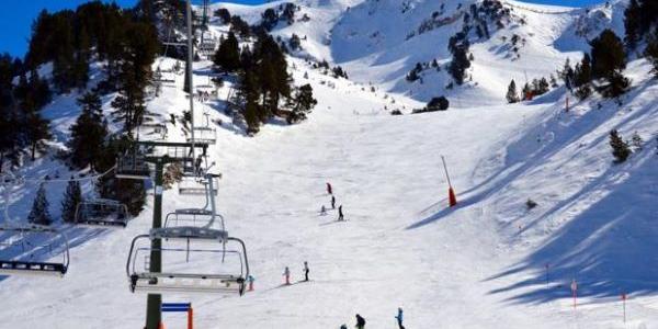 Una montaña nevada en la que descienden diversos esquiadores y a la izquierda se deja ver un tele-silla 