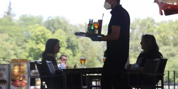 Un camarero protegido con mascarilla atiende a una mesa de una de las terrazas abiertas en el Parque de El Retiro 