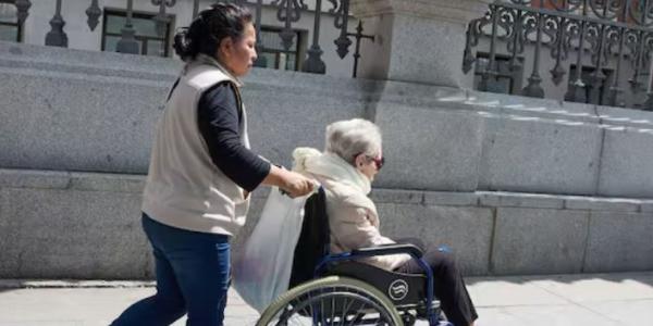 Mujer extranjera cuidado de una persona dependiente en silla de ruedas
