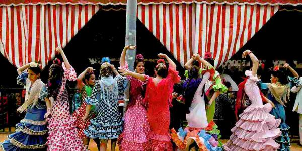 Varias mujeres vestidas de flamenca bailan frente a una caseta