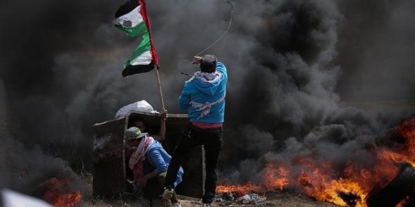 Joven palestino salta detrás de la bandera de su país rodeado de humo y llamas