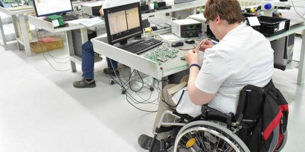 Persona con discapacidad trabajando en una fábrica de ensamblaje de componentes electrónicos. 