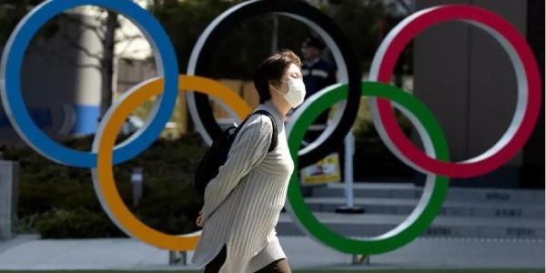 Juegos Olímpicos: Una mujer con mascarilla pasa frente a los anillos olímpicos en el Museo Olímpico de Japón, en Tokio, el 13 de marzo de 2020