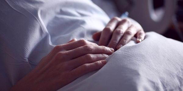 Las manos de un paciente que descansa en la cama de un hospital