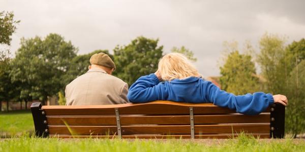 Un señor mayor y una mujer adulta sentados en un banco de espaldas
