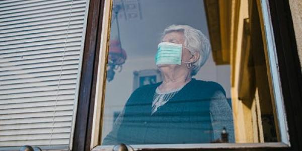 Persona mayor con mascarilla en la ventana de su casa / Vuk Saric / Shutterstock