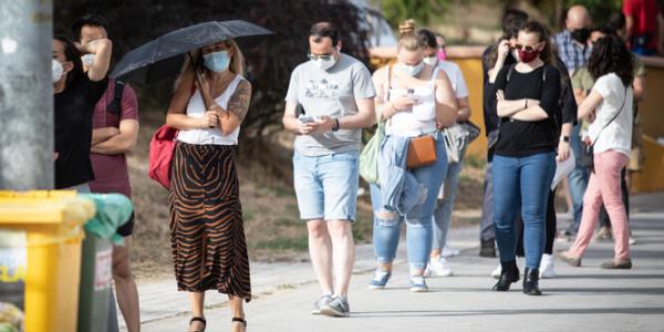 Una mujer se protege del sol con un paraguas en la cola de la vacunación