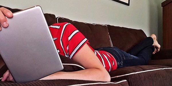 Persona tumbada en el sofá con una tablet, en mala postura