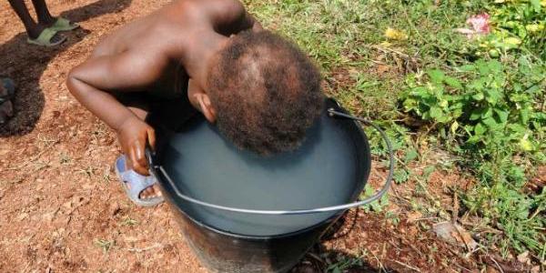 Un niño intenta beber agua turbia en un cubo